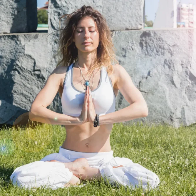 Woman sitting in a peaceful meditation pose outdoors, hands in prayer position, representing the inward transformation of matrescence
